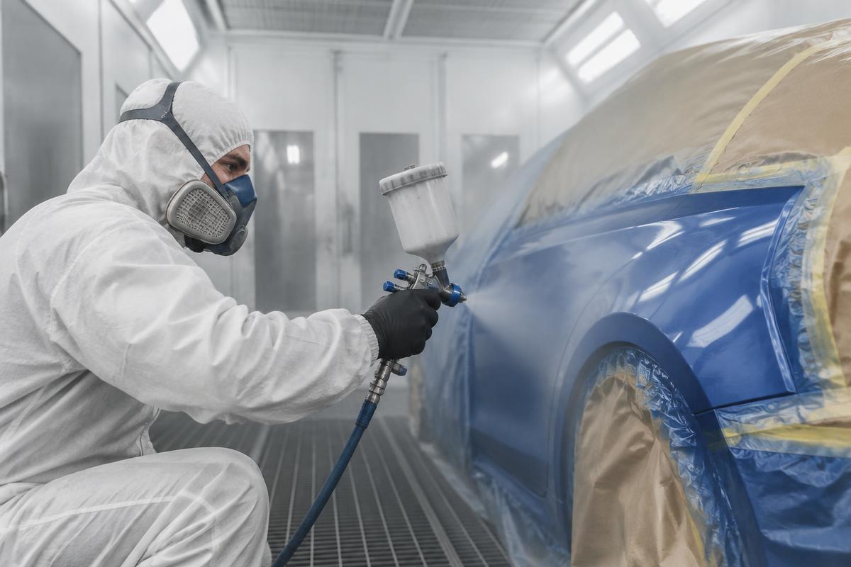 Painter spraying a glossy automotive finish on a car panel in the spray booth